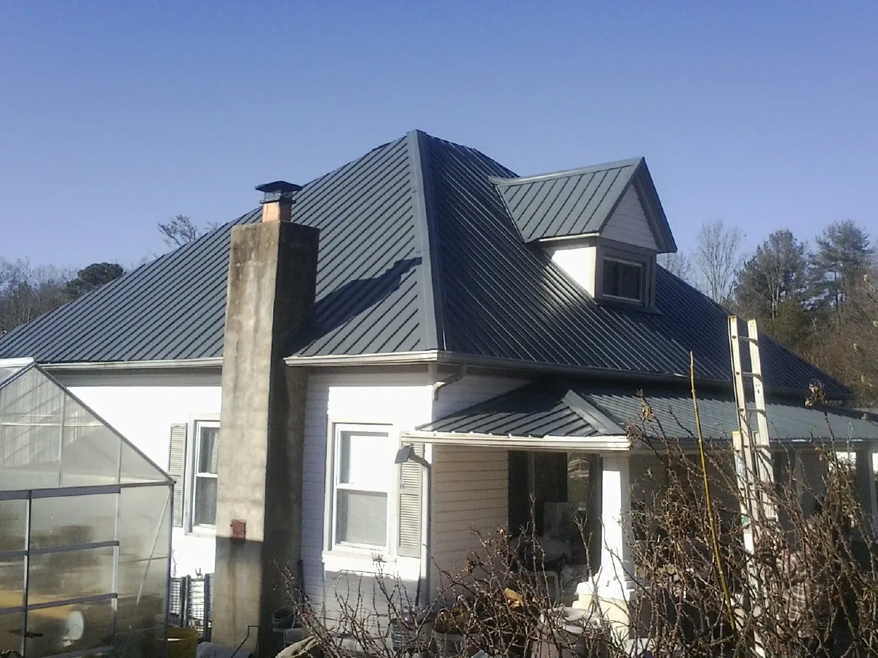 Dark blue standing seam metal roof on a white farmhouse with dormer — Slate & Tile Roof Repair by Roofing Brothers in Olar