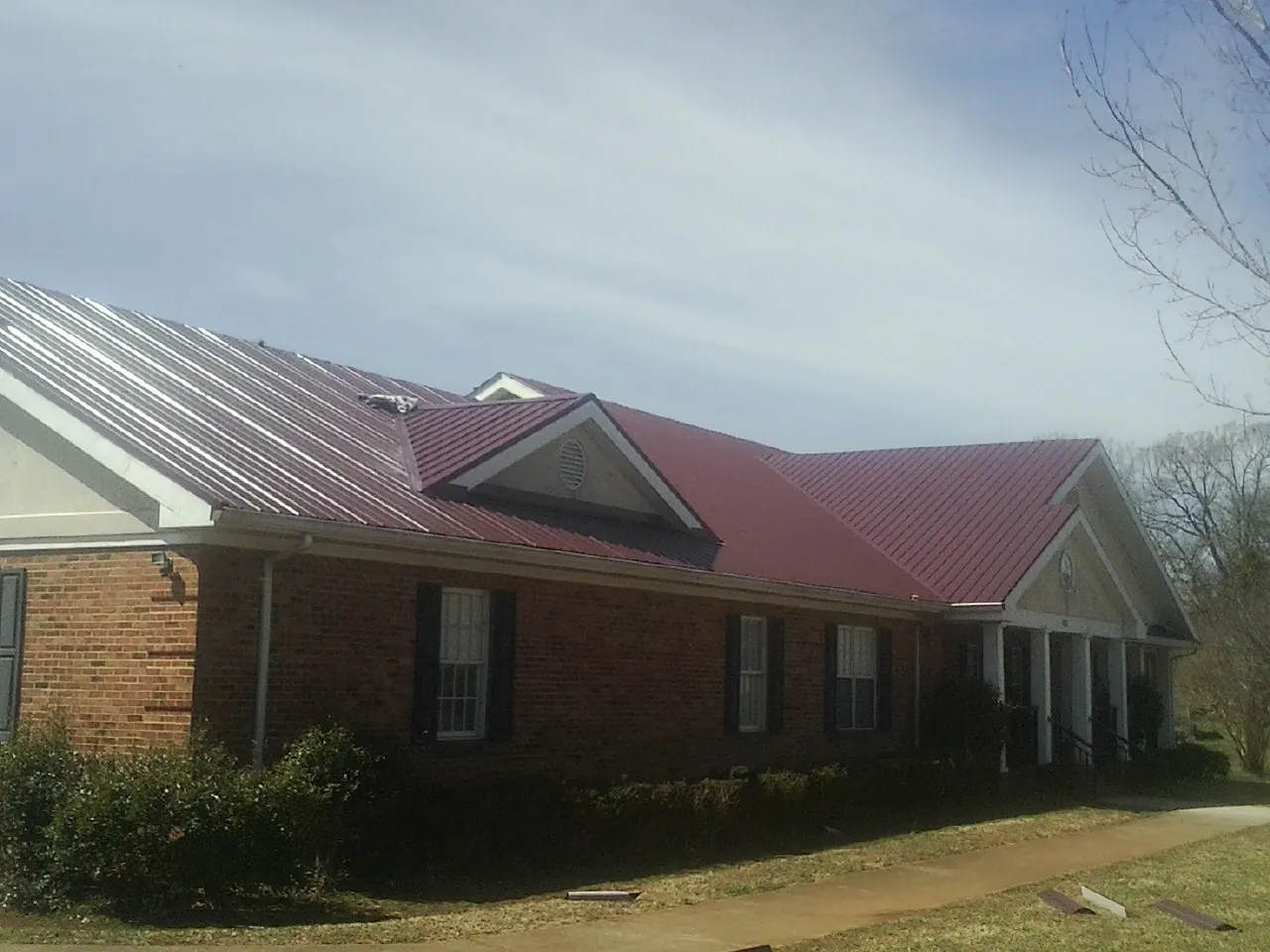 Red metal roof with gabled entries on a long brick building, from a Hail Damage Roof Repair job in Olar