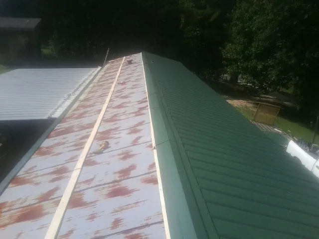 Old rusted panels beside newly installed green metal roofing — Wind Damage Roof Repair by Roofing Brothers in Olar
