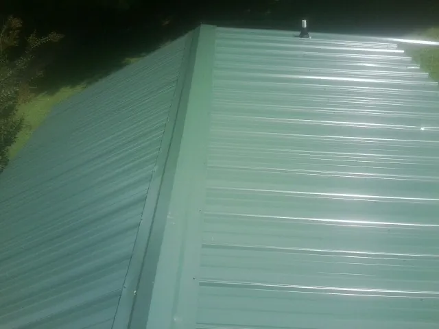 New green metal panels meeting at the ridge of a roof — Flat Roof Repair work by our crew in Olar