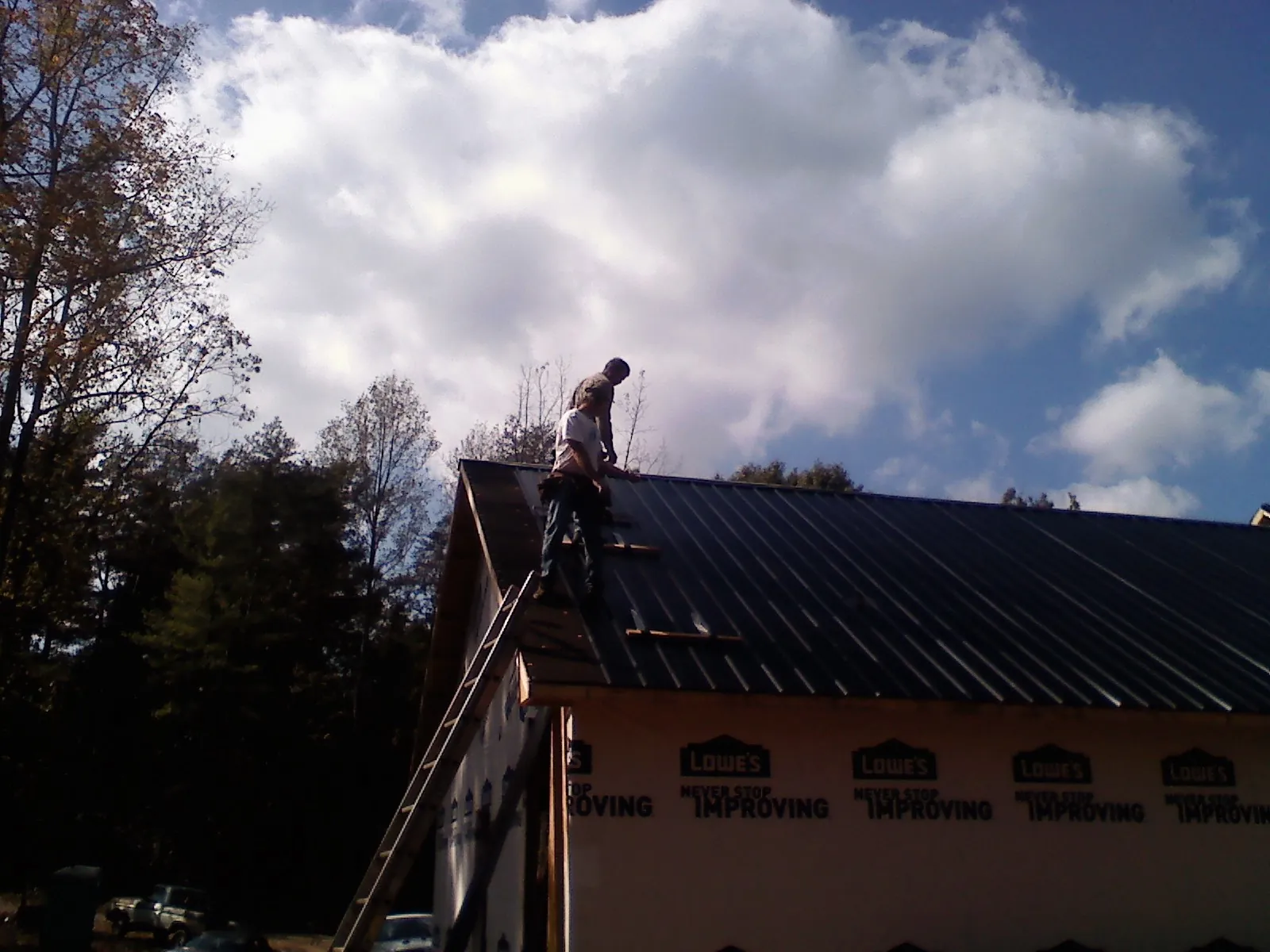 Roofer fastening dark metal panels high against a cloudy sky, from a Roof Inspection job in Olar