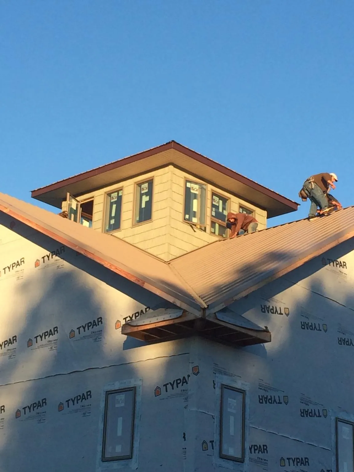 Roofers working around a rooftop cupola on a new metal roof at sunset in Olar